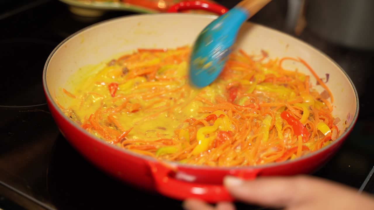 Chef with the help of wok spatula stirring the gravy of bell papers and other veggies in frying pan.