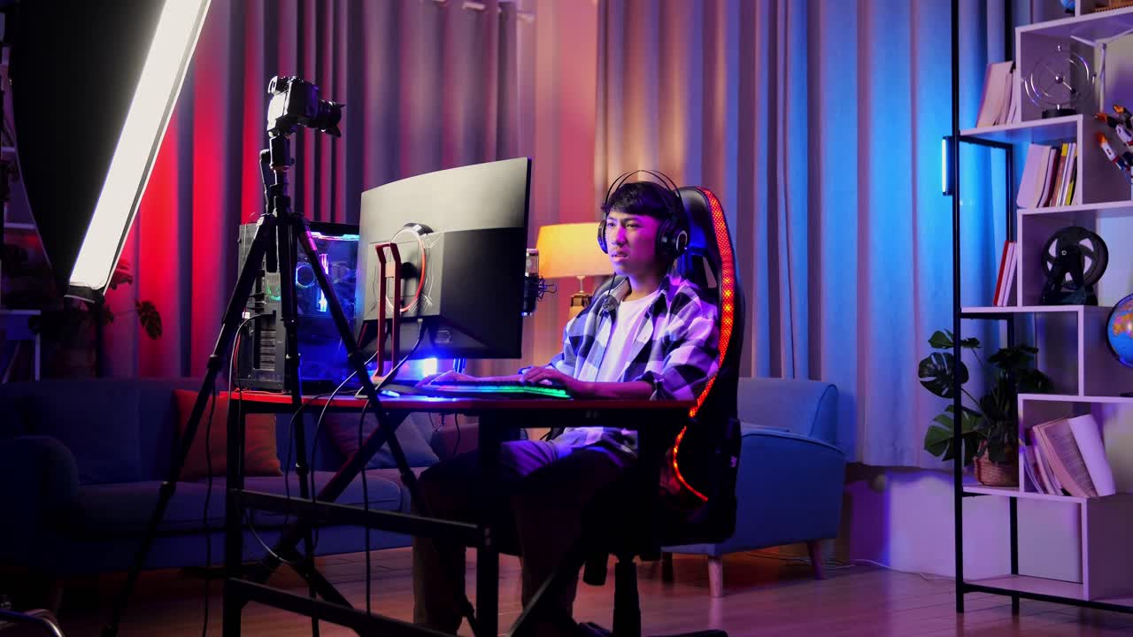 asian boy streamer con dolor de espalda mientras juega un juego a través de la red en una computadora personal. videojuego de transmisión en vivo, escritorio iluminado por luz de tira de led rgb