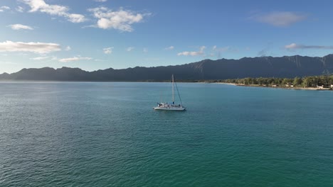 60-fps-Drohnenluftaufnahmen-Des-Ozeans-Von-Hawaii-Mit-Katamaran-Im-Blauen-Wasser-Mit-Waimanalo-Bergen-Im-Hintergrund-Und-Vielen-Bäumen-Am-Mittagsblauen-Himmel