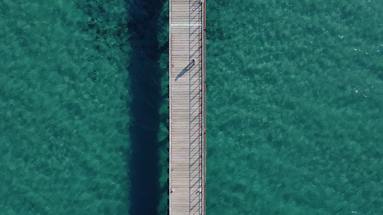 Vista aerea con drone di una persona che cammina lungo un lungo molo di legno circondato da scintillanti acque tropicali