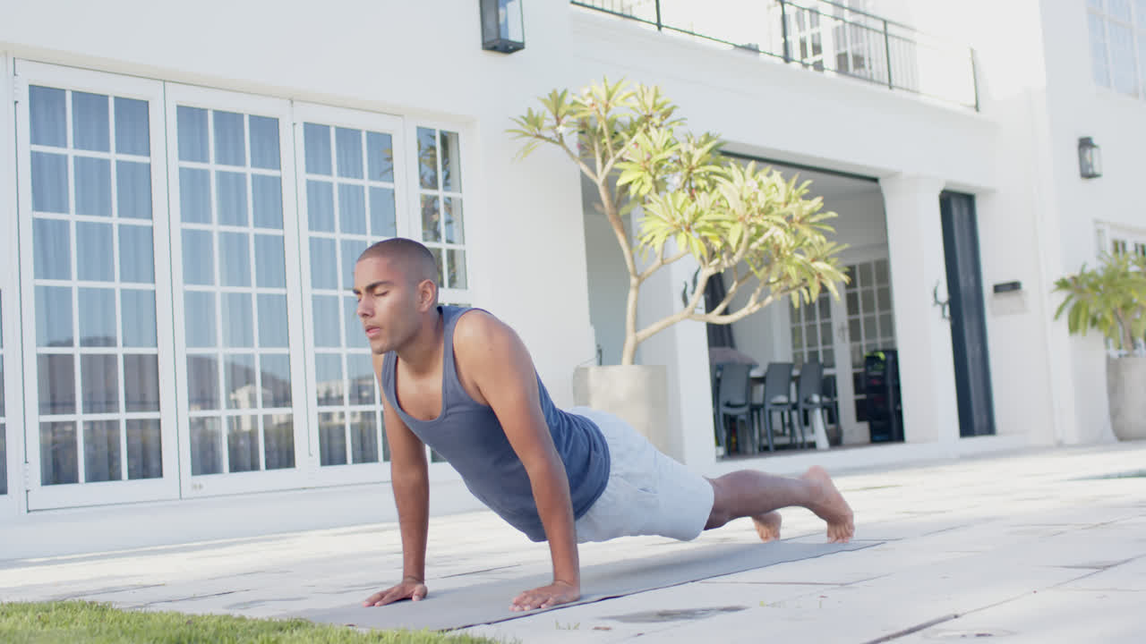 Focused biracial man practicing yoga in sunny garden, slow motion