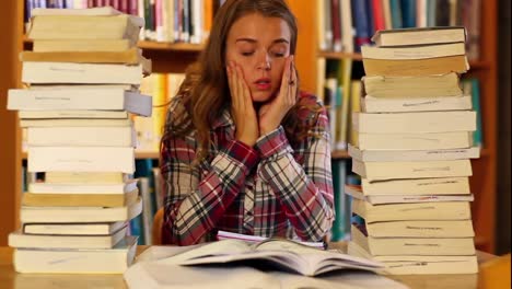 estudiante estresado estudiando y tomando notas en la biblioteca rodeado de libros