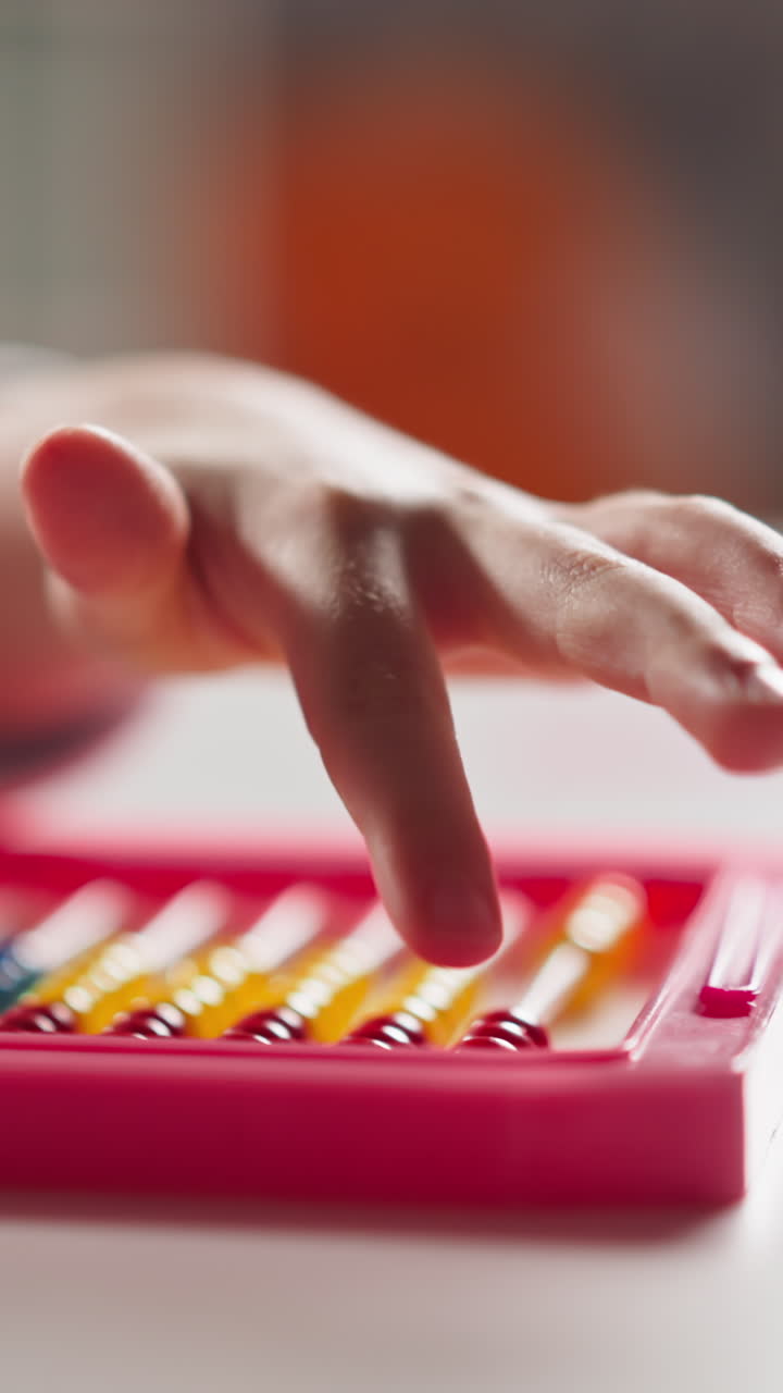 Little girl pupil hand counts moving small beads on colorful toy abacus at mental arithmetics lesson at home extreme closeup slow motion