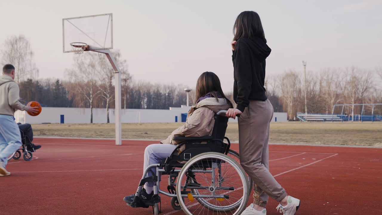 mujer discapacitada en silla de ruedas y su amiga mirando a sus amigos jugando al baloncesto 1