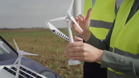 team of caucasian and latin engineers standing on wind turbine field and discussing over project.