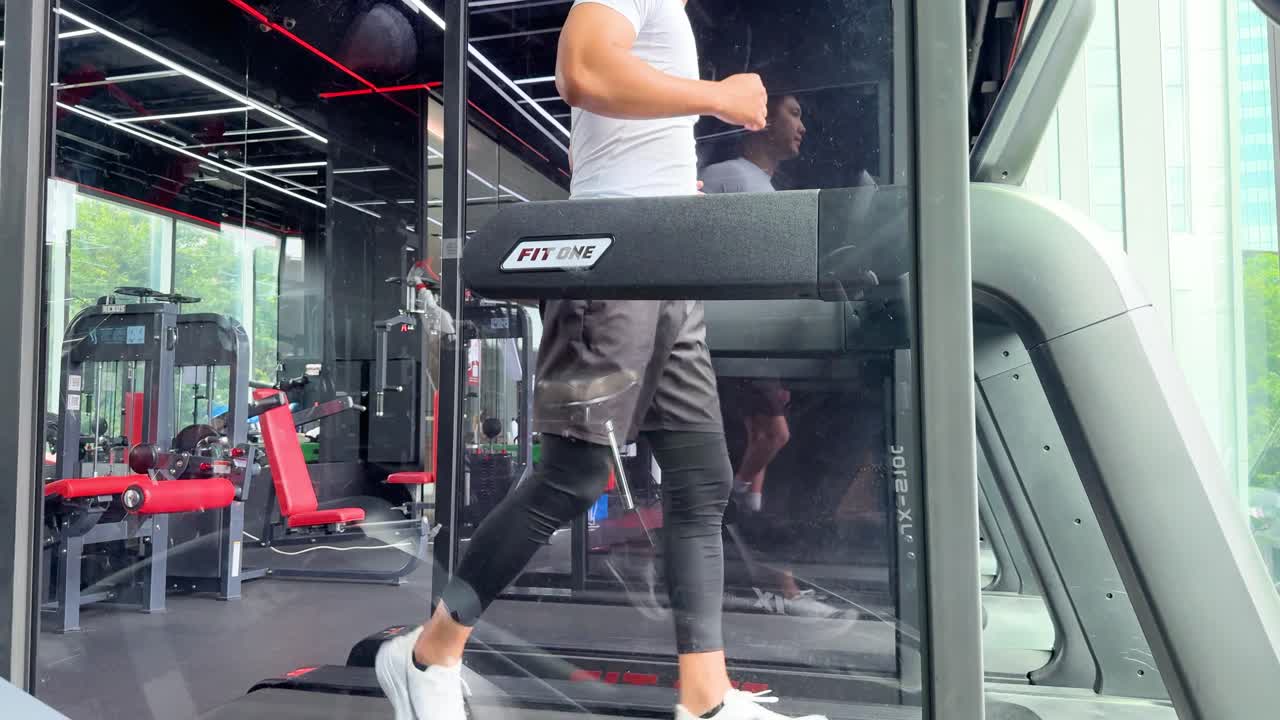 Athletic man runs on treadmill in bright, contemporary gym with large windows and natural light