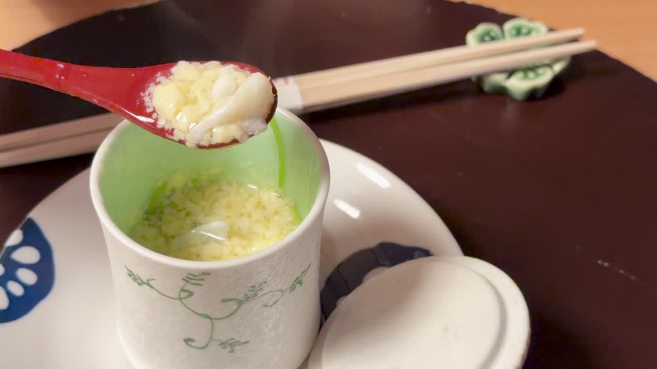 金沢で、湯気の立つ風味豊かな茶碗蒸しが赤いスプーンで持ち上げられているクローズアップショット