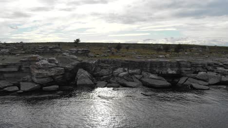 Drone flying away from rocky coastline near Asunden Rauk Field Sweden