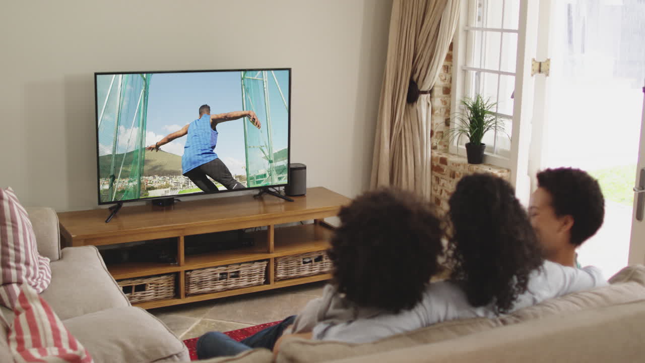 Composizione di famiglia felice seduta insieme a casa che guarda un evento di atletica leggera di lancio del disco in TV.