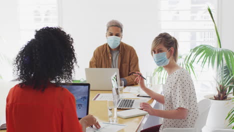 Office-colleagues-wearing-face-masks-discussing-in-meeting-room-at-office