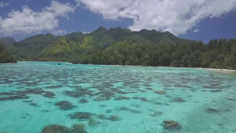 drone flying over shallow bay with clear tropical water in french polynesia