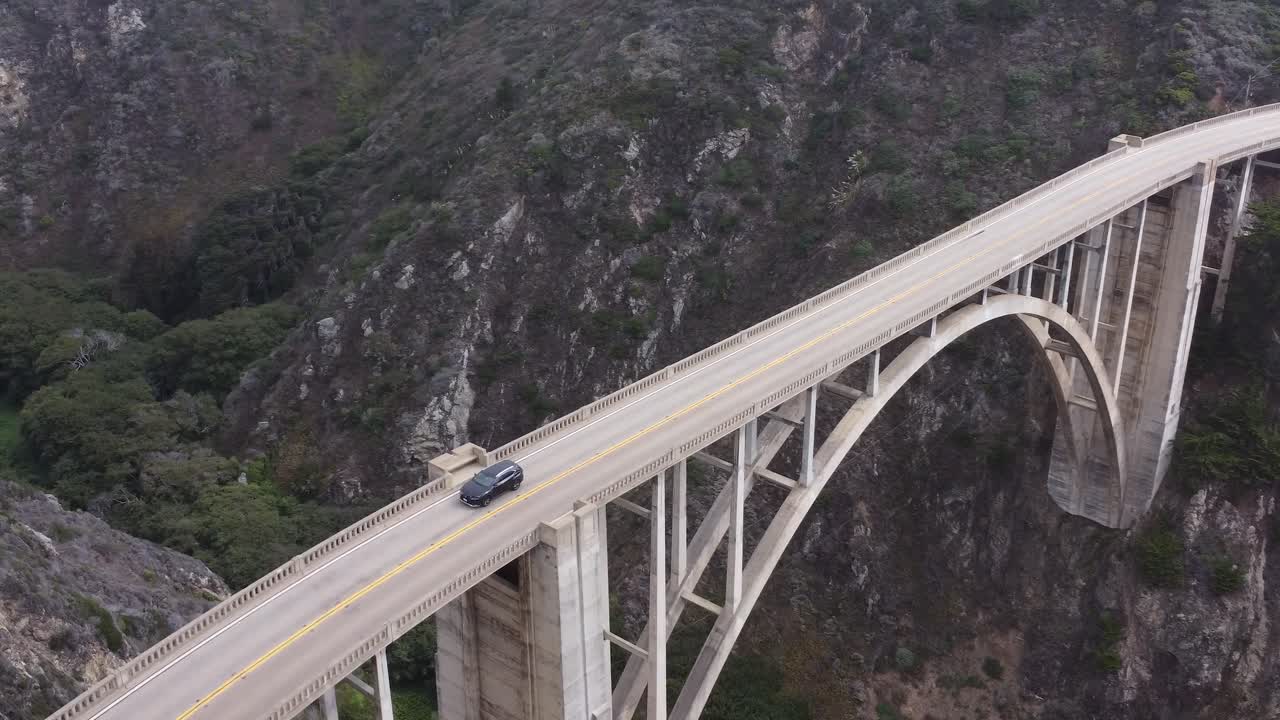 Rotation drone shot of a bridge between mountains with cars driving.