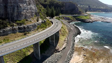 curve road by the cliff edge with vehicles on journey across grand pacific drive at sea cliff bridge, nsw australia