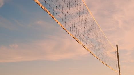 SLOW-MOTION-LOW-ANGLE-CLOSE-UP-LENS-FLARE:-Young-female-volleyball-players-pass-and-spike-the-ball-over-the-net-on-a-sunny-summer-evening.-Fit-Caucasian-girls-playing-beach-volleyball-at-sunset.