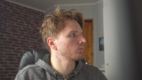 A-young-man-with-wild-disheveled-hair-is-reading-his-computer-monitor