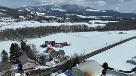 push in drone shot flying above snow covered houses and fields, with ski area and mountain town in distance