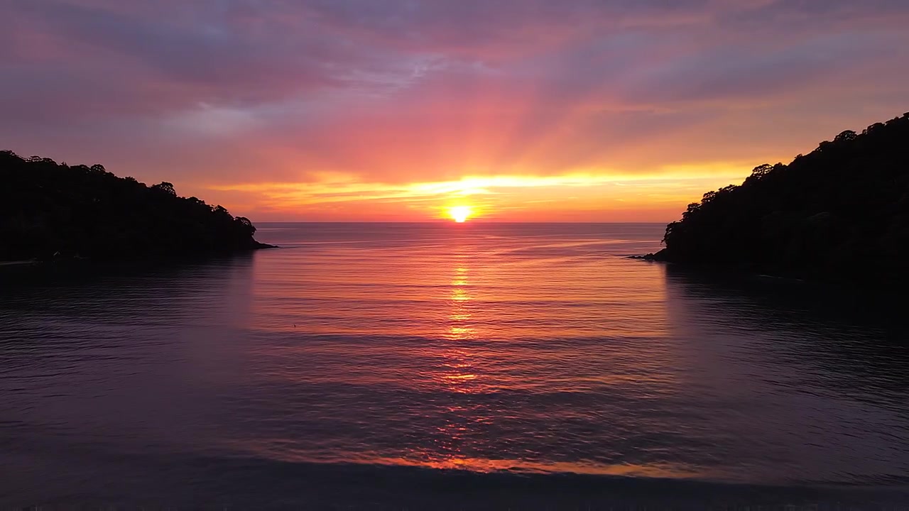 Vibrant Sunset Over Tropical Bay Framed by Lush Greenery