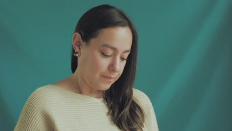 medium shot of a young woman in focus on a professional recording set, with a solid turquoise background.