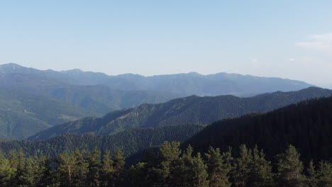 Revealing-aerial-shot-of-a-dense-forest,-jungle,-and-mountain-range-on-a-clear-blue-day