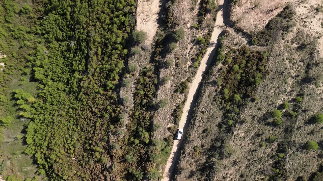 vista aérea de un coche blanco conduciendo a lo largo de un camino de tierra rodeado de almendros, olivos y vegetación en sierra calderona