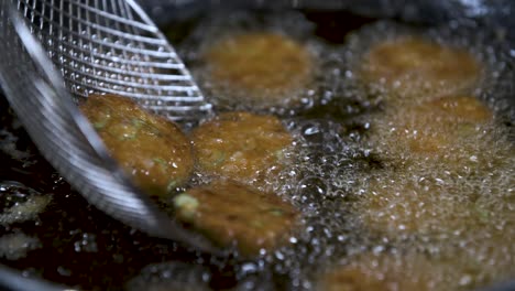 deep frying tod man pla thai fish cakes in hot oil with skimmer - close up