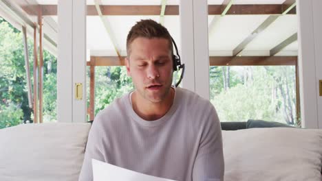 Retrato-De-Un-Hombre-Caucásico-Usando-Auriculares-De-Teléfono-Hablando-Mirando-A-La-Cámara-Mientras-Está-Sentado-En-El-Sofá