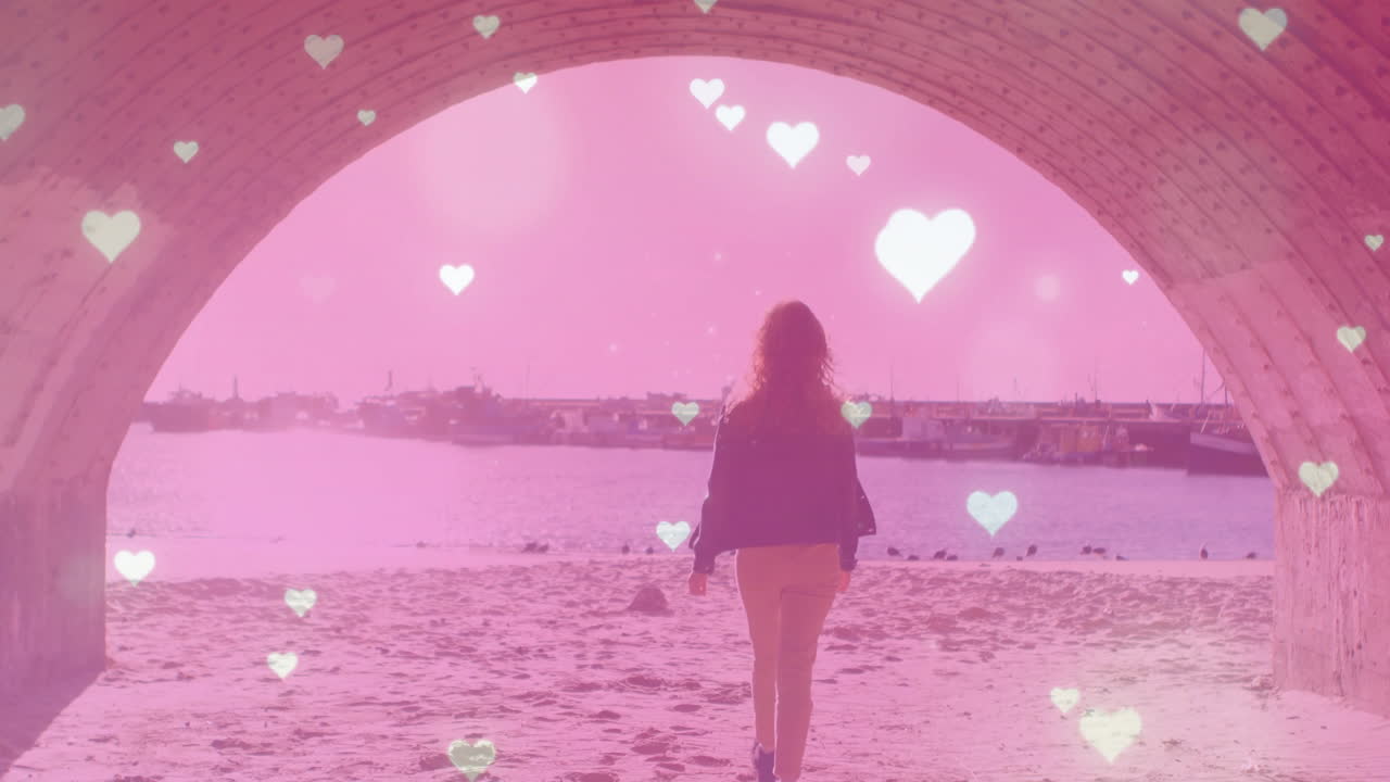 Person walking under archway towards beach with heart animations overlay