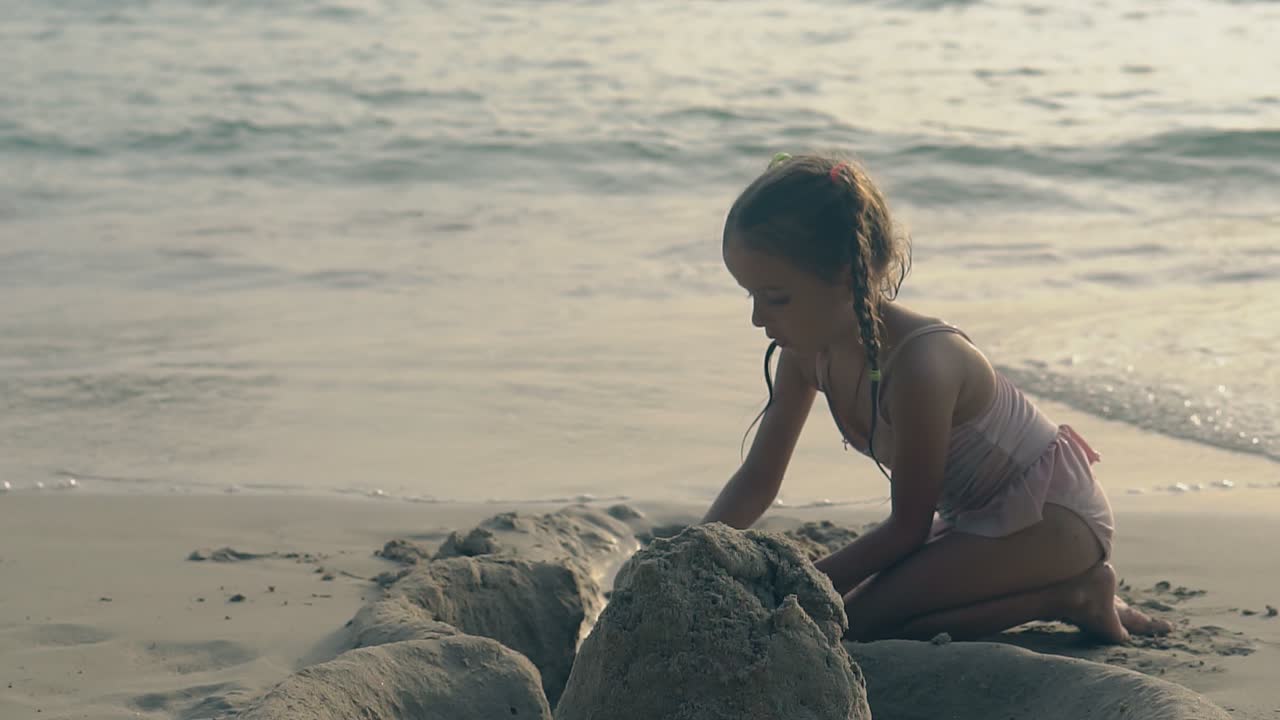 작은 소녀는 모래를 파고 서프 라인에 성을 짓습니다.