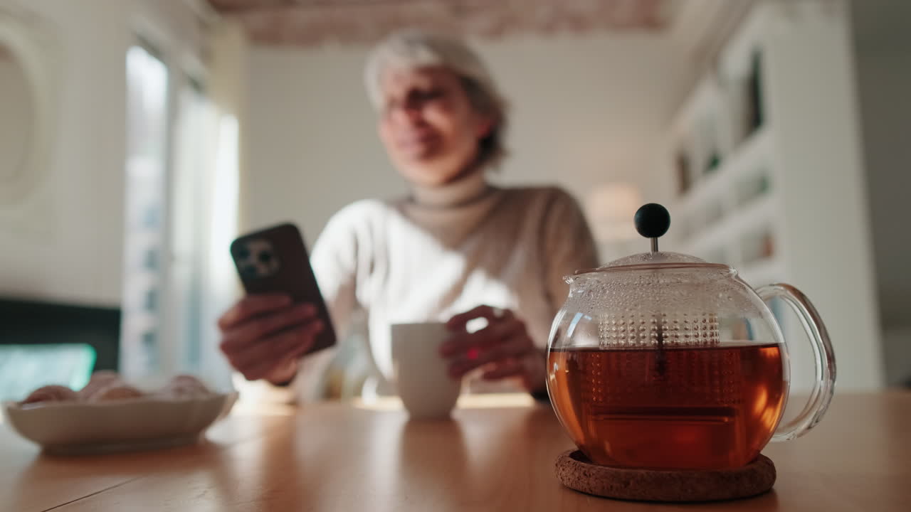 Donna rilassata che naviga sullo smartphone mentre beve il tè a casa