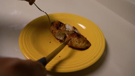 cortar una pechuga de pollo a la barbacoa con un tenedor y un cuchillo en un plato amarillo