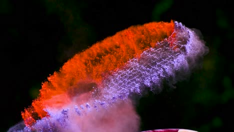 tennis racket covered in red, blue and purple powder being hit by a tennis ball in slow motion