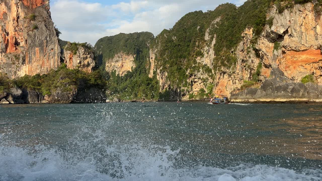 Snabbgående longtailbåt som färdas över turkost vatten mellan Ao Nang Beach och Railay Beach i Krabi, Thailand, med kalkstensklippor och tropisk kustlinje.