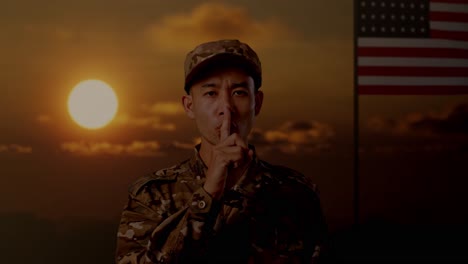 close up of asian man soldier looking at camera and making shh gesture while standing with flag of the united states, sunset time