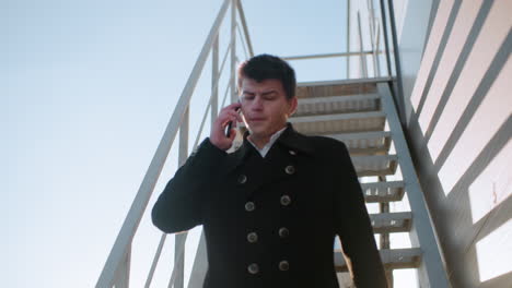 man in black coat descending staircase on phone call holding briefcase, nodding while conversing under sunlight, sunlight reflects brightly in background