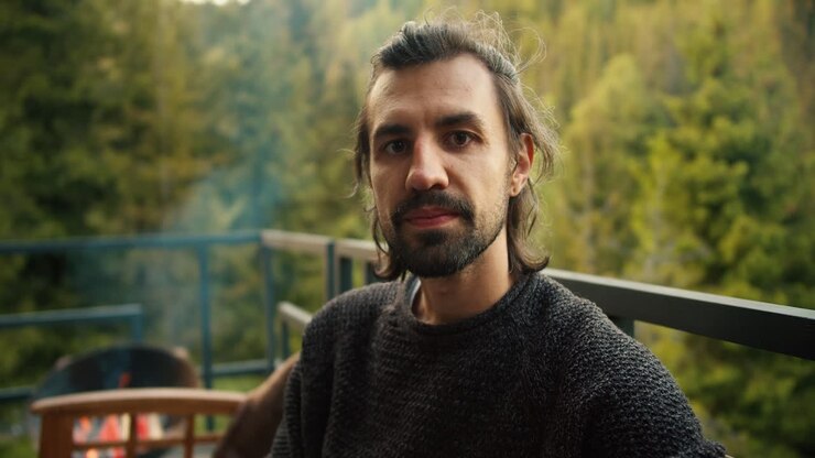 Portrait of a serious young man at a picnic outside the city. Overview of a guy who is sitting on a devan with a view of the mountains and coniferous forest