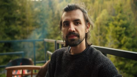 Portrait-of-a-serious-young-man-at-a-picnic-outside-the-city.-Overview-of-a-guy-who-is-sitting-on-a-devan-with-a-view-of-the-mountains-and-coniferous-forest