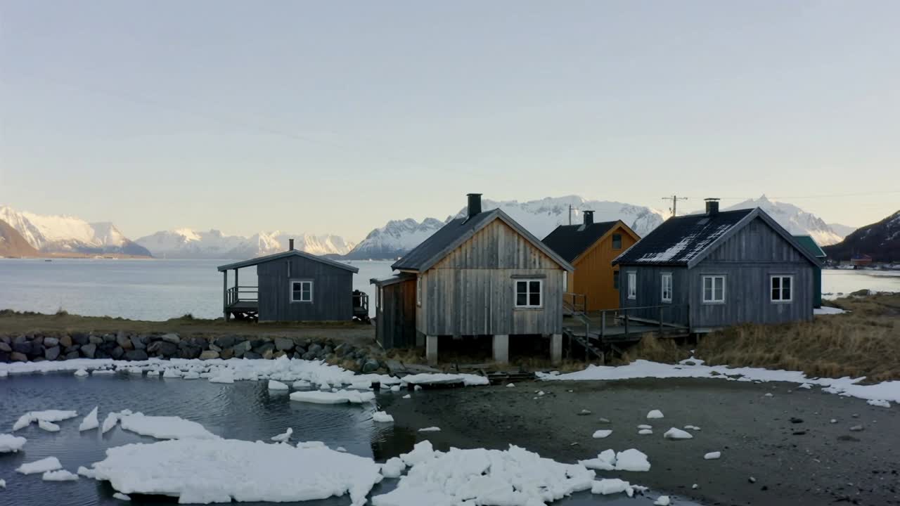 Panorering av kamera som avslører en klynge av trehus langs strandlinjen ved fjorden, som viser is midt på fjorden