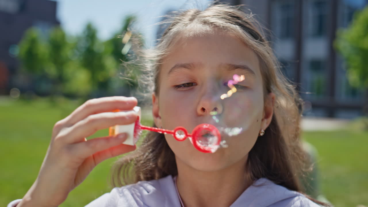 Playful girl blowing soap bubbles on meadow portrait. Cheerful child playing
