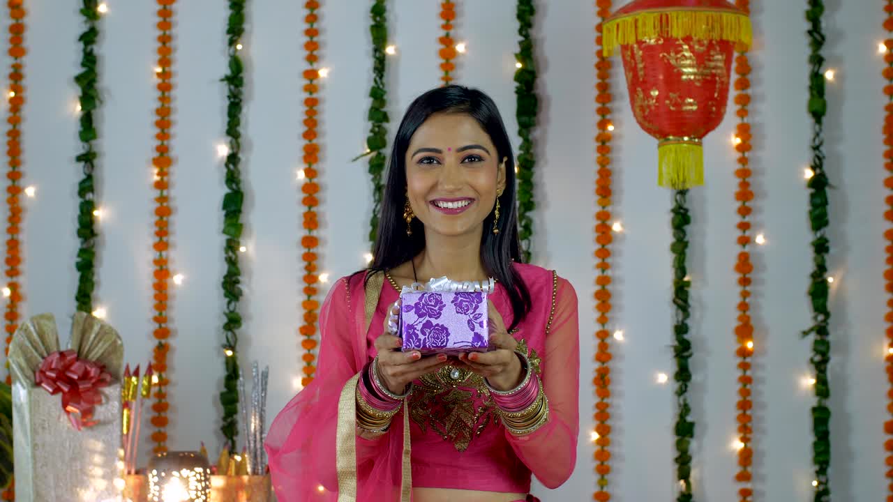 joven hermosa sonriendo felizmente y mostrando un regalo a la cámara - festival de diwali