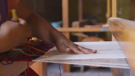 a woman weaving yellow wool through a loom to create a tapestry