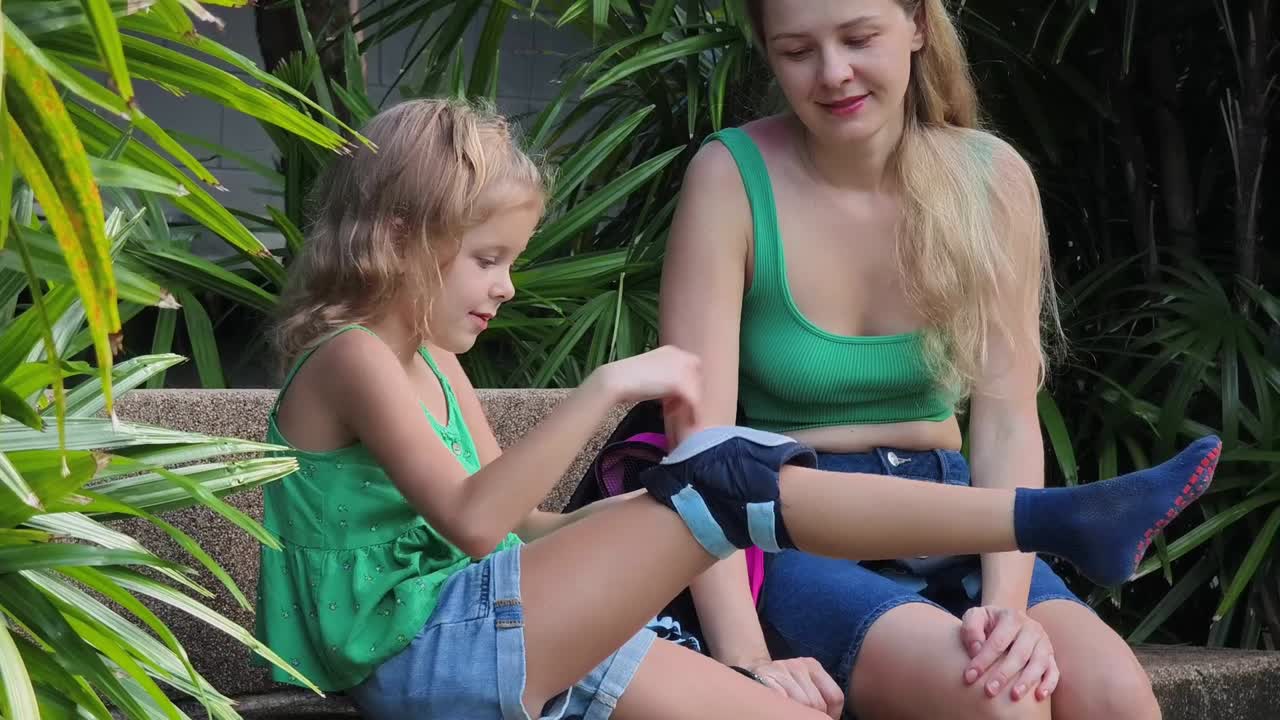 어머니 는 딸 이 무 보호 장치 를 착용 하는 데 도움 을 주고 있다