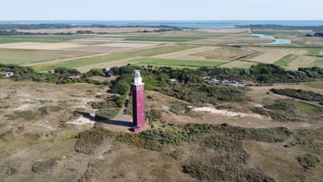 drone rotates around red lighthouse in the netherlands on a beautiful bright sandy beach with sunny weather