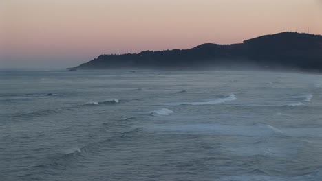 mist lies above the ocean waves rolling towards shore beneath a pastel sky
