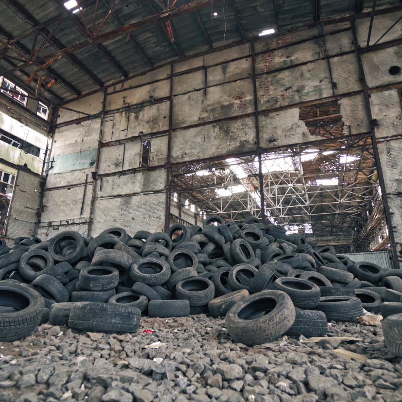 Big old empty factory with garbage and a pile of used rubber tyres inside. Tires that are no longer suitable for use on vehicles in a damaged plant.