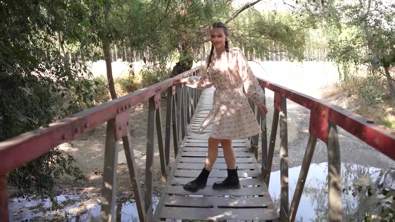 Una giovane donna affascinante passeggia casualmente su un ponte rustico, circondata da una natura splendida.