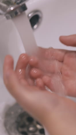 cute little girl washes hands and face with clean water at ceramic sink in light bathroom at home closeup