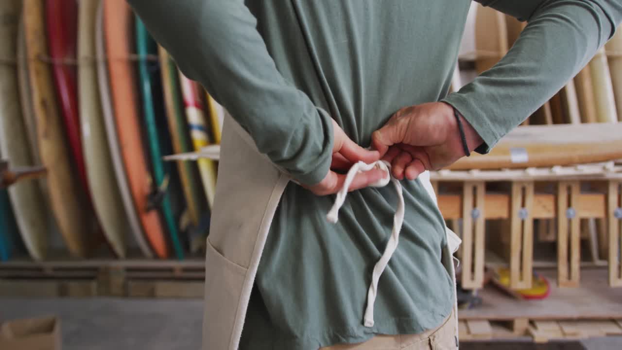 Caucasian male surfboard maker putting on a protective apron in his studio