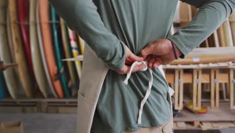 caucasian male surfboard maker putting on a protective apron in his studio