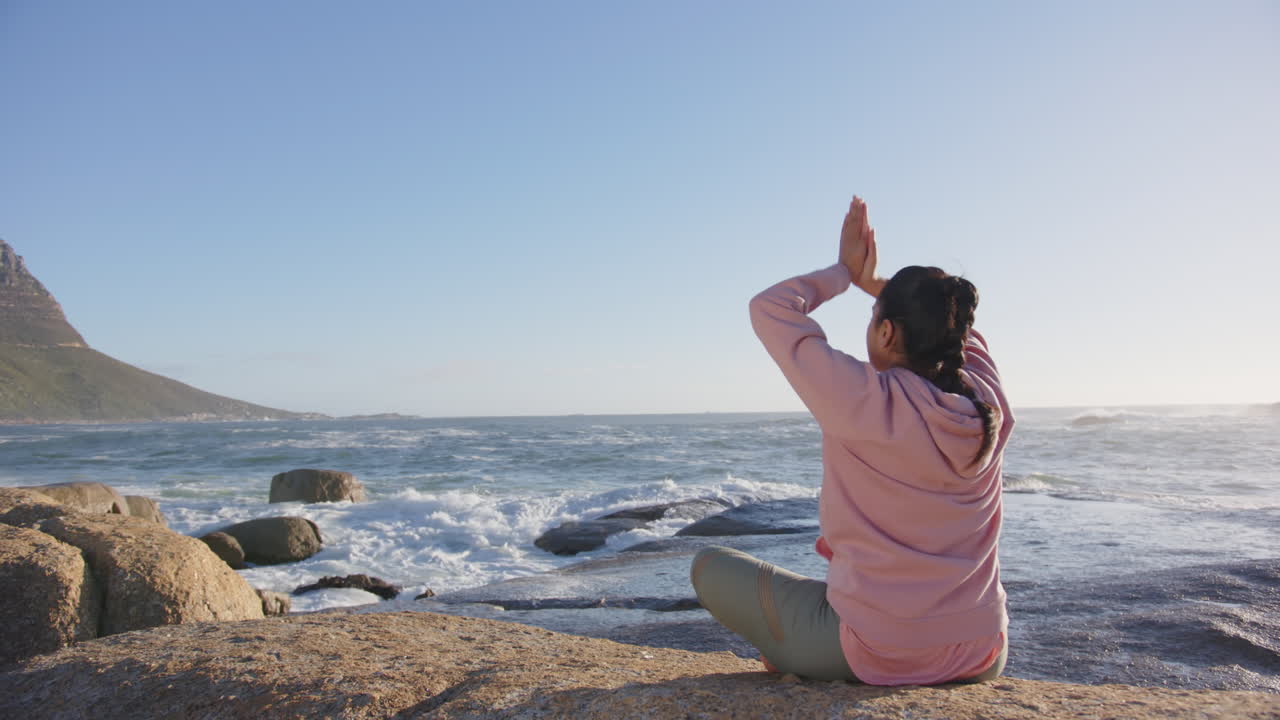 Practicing mindfulness on rocky shore, asian woman meditating by ocean