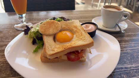 Tasty-breakfast-sandwich-with-egg,-bacon-and-salad-with-coffee-and-fresh-orange-juice,-morning-brunch,-4K-shot